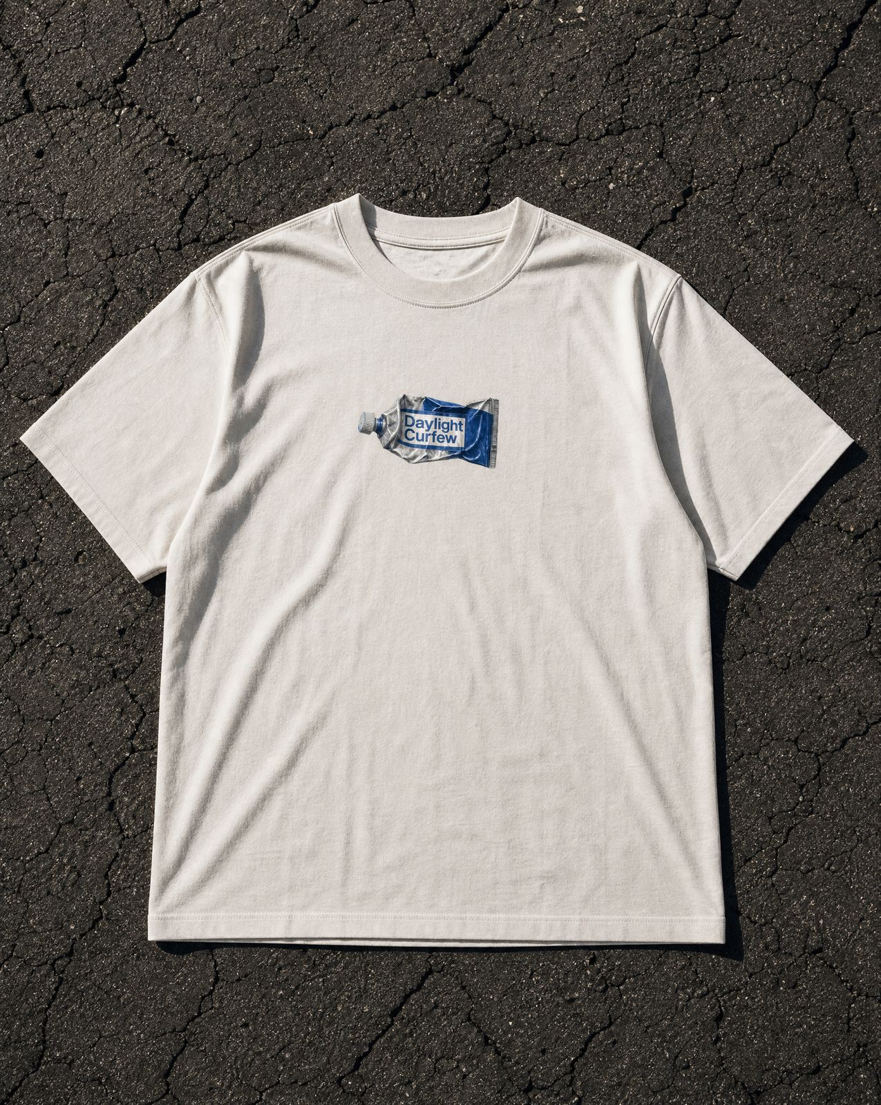 DLC Paint Tube Tee Ivory, overhead flatlay on asphalt