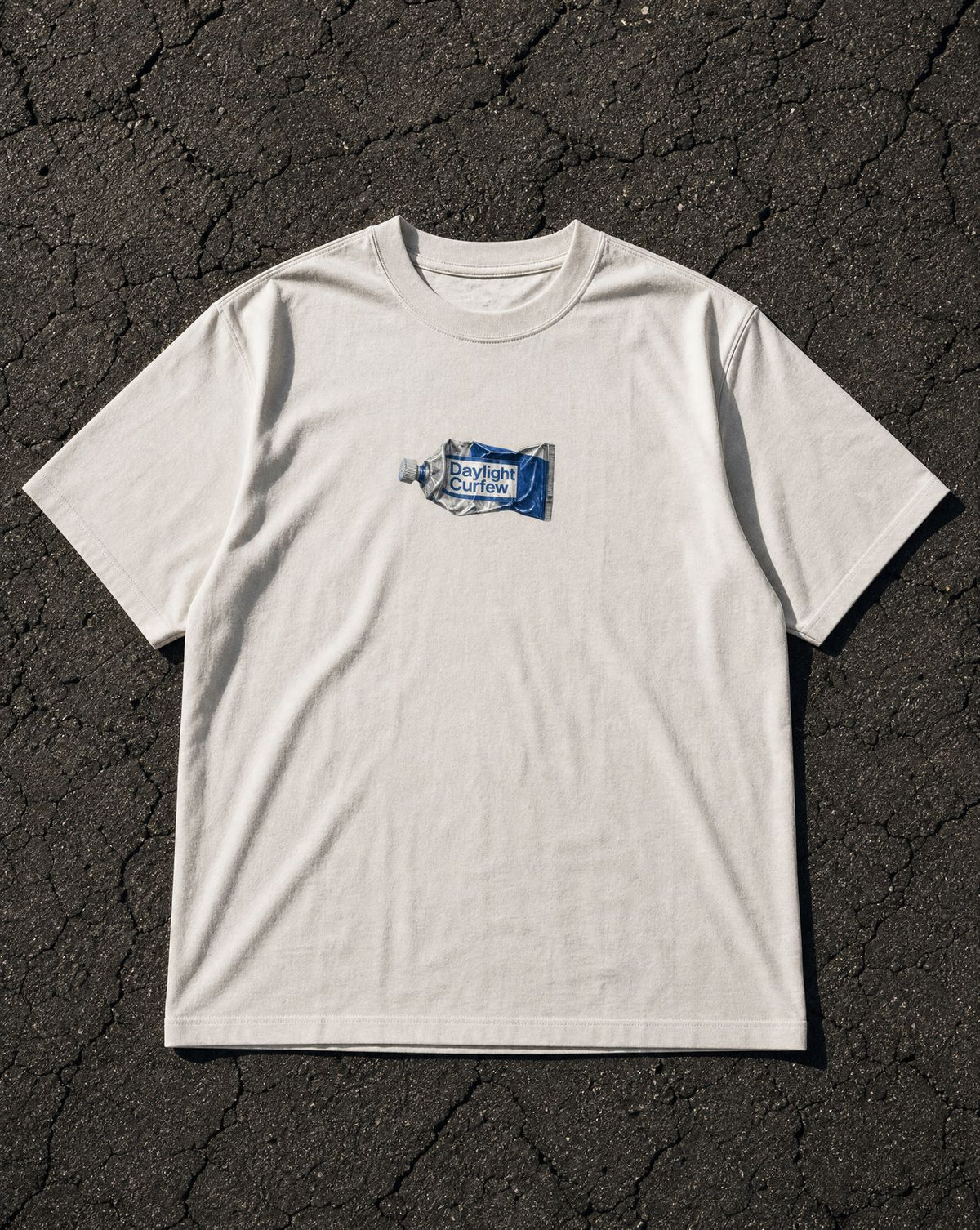 DLC Paint Tube Tee Ivory, overhead flatlay on asphalt